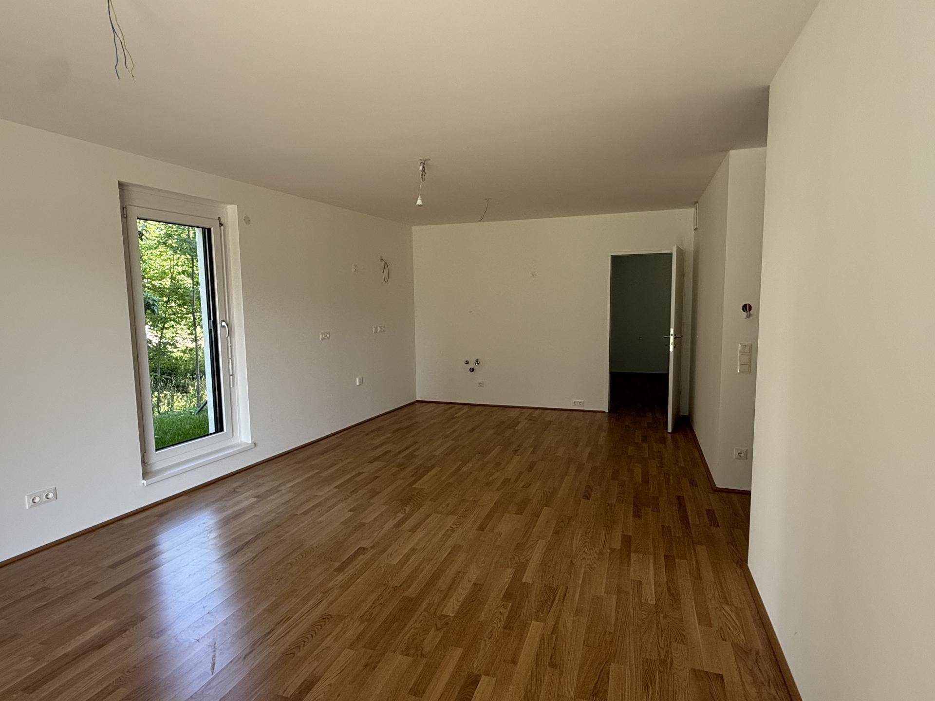 Geräumiges Wohnzimmer mit Parkettboden und großem Fenster mit Blick ins Freie und viel Licht.
