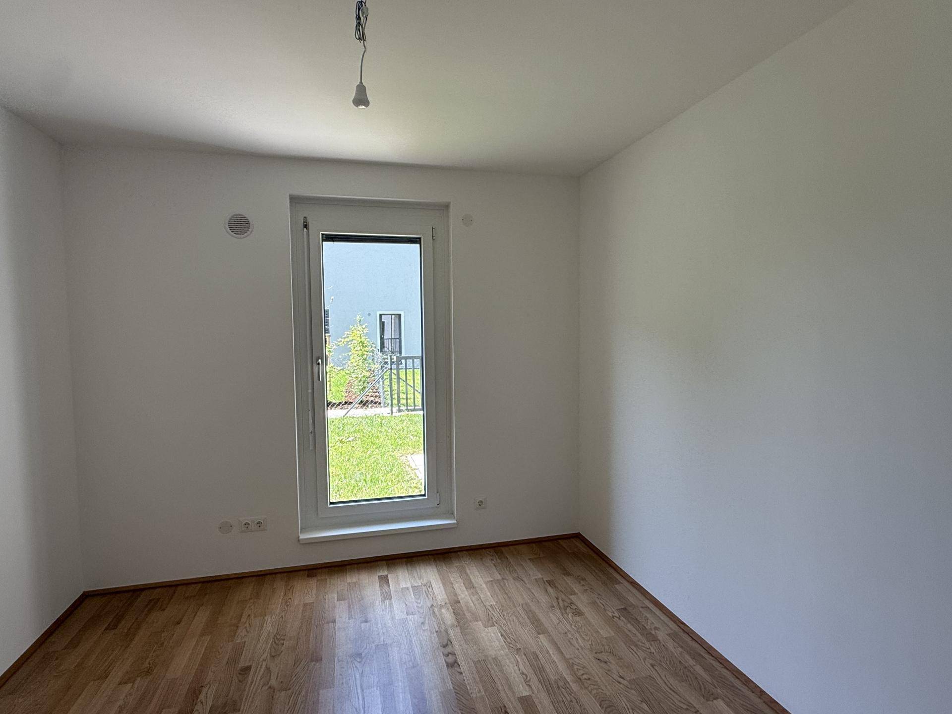 Freundliches Zimmer mit Holzboden und Fenster, das viel Tageslicht hereinlässt und Ausblick bietet.