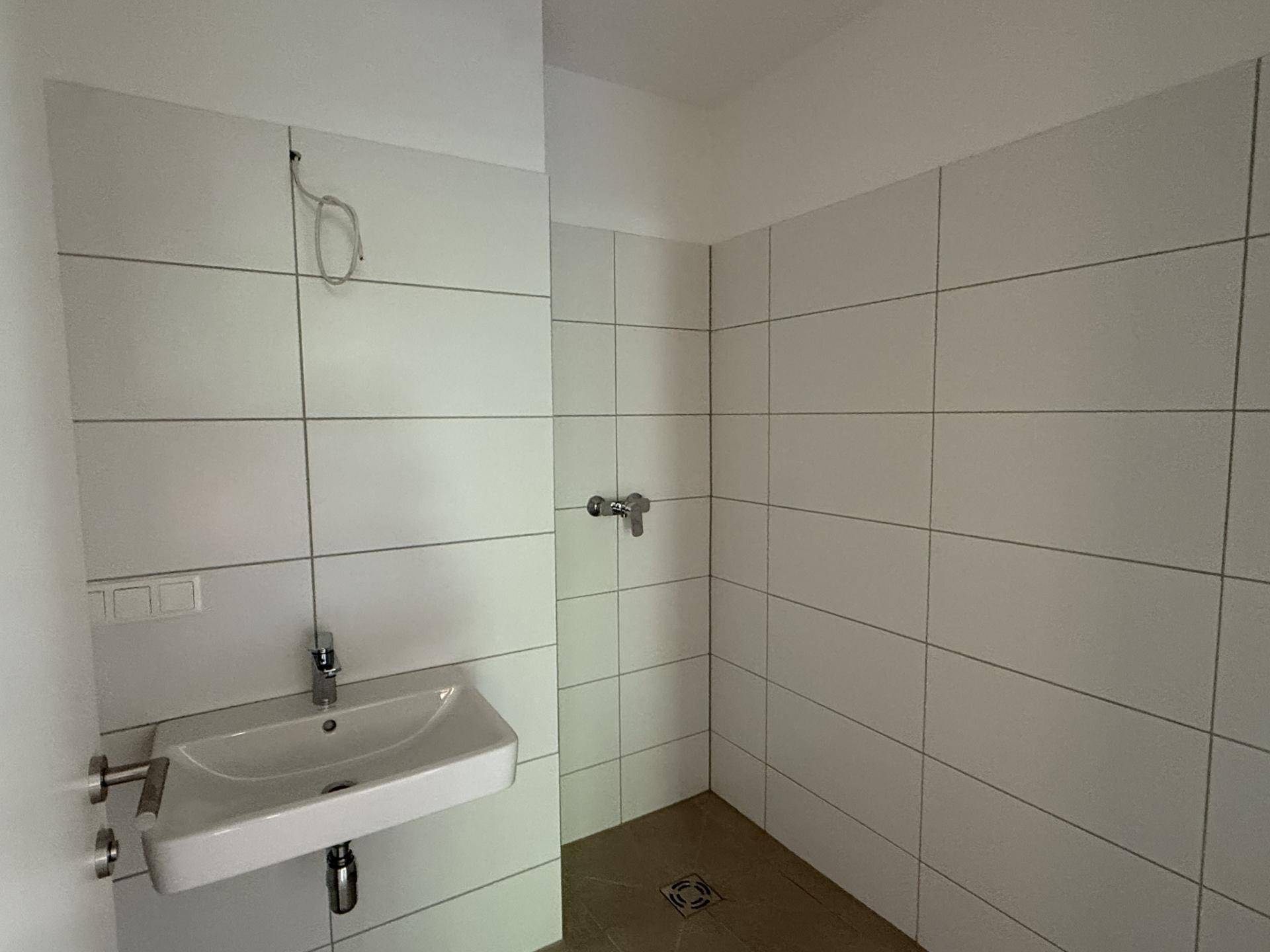 Modern gefliestes Badezimmer mit Duschbereich und Waschbecken, hell und funktional gestaltet.