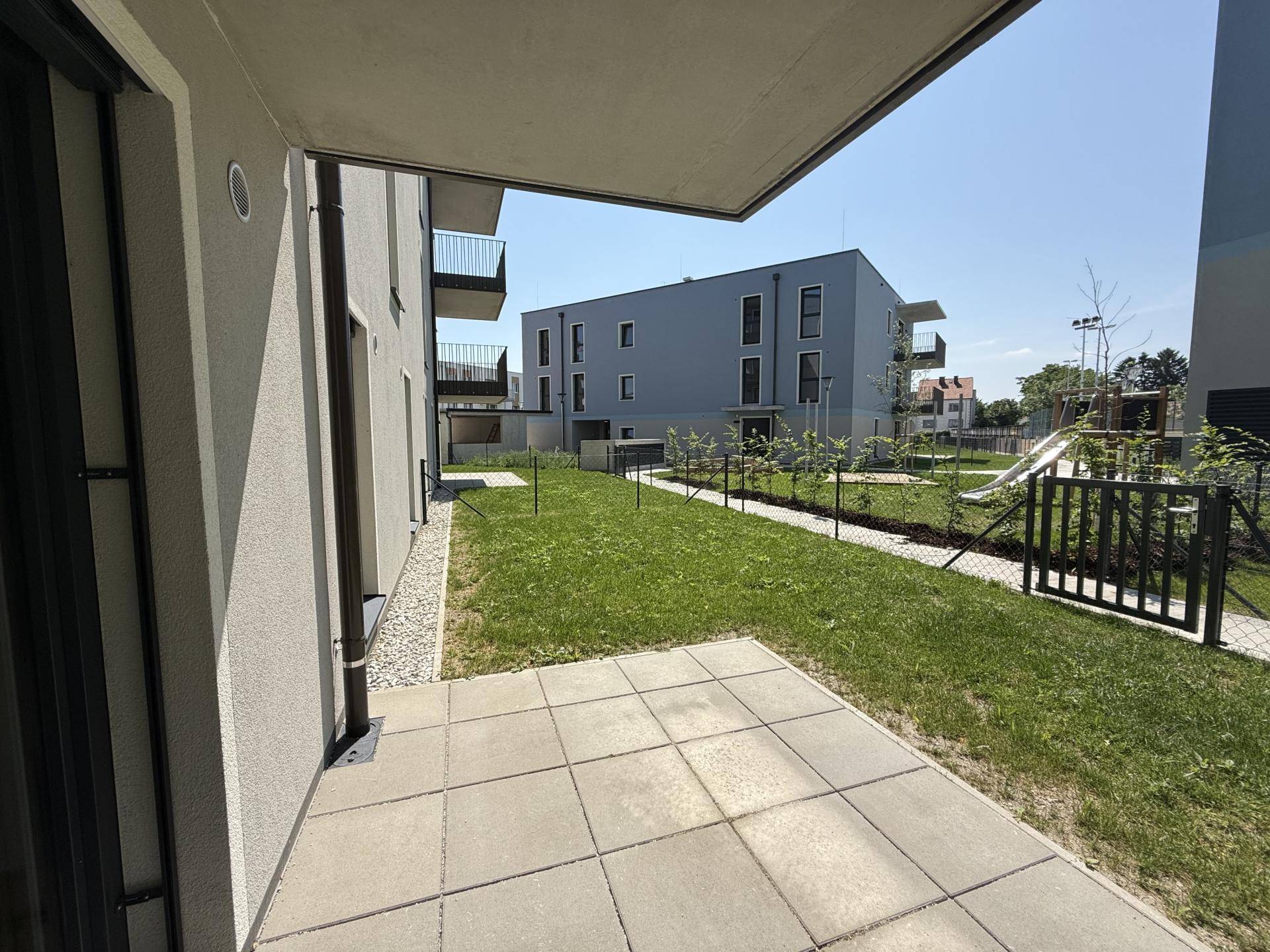 Sonniger Garten mit Terrasse und Blick auf die moderne Architektur des Wohnkomplexes an einem hellen Tag.