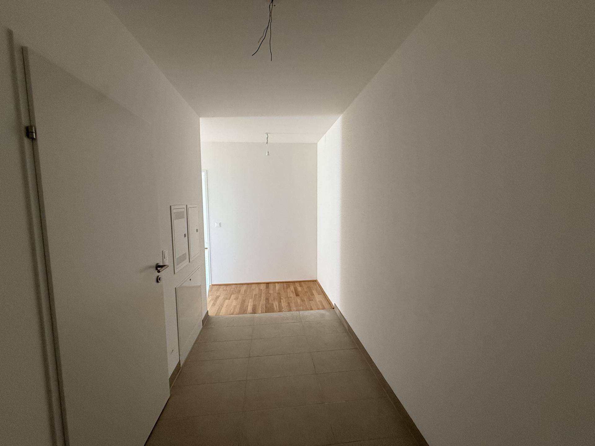 Heller Flur mit Fliesenboden und Zugang zu weiteren Räumen im Neubau.