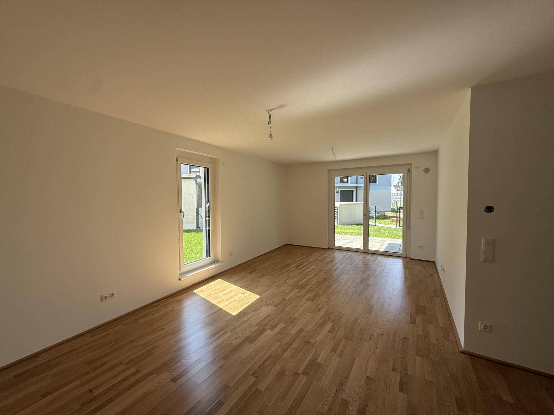 Geräumiges, helles Zimmer mit Holzboden und zwei Zugängen zum Gartenbereich.