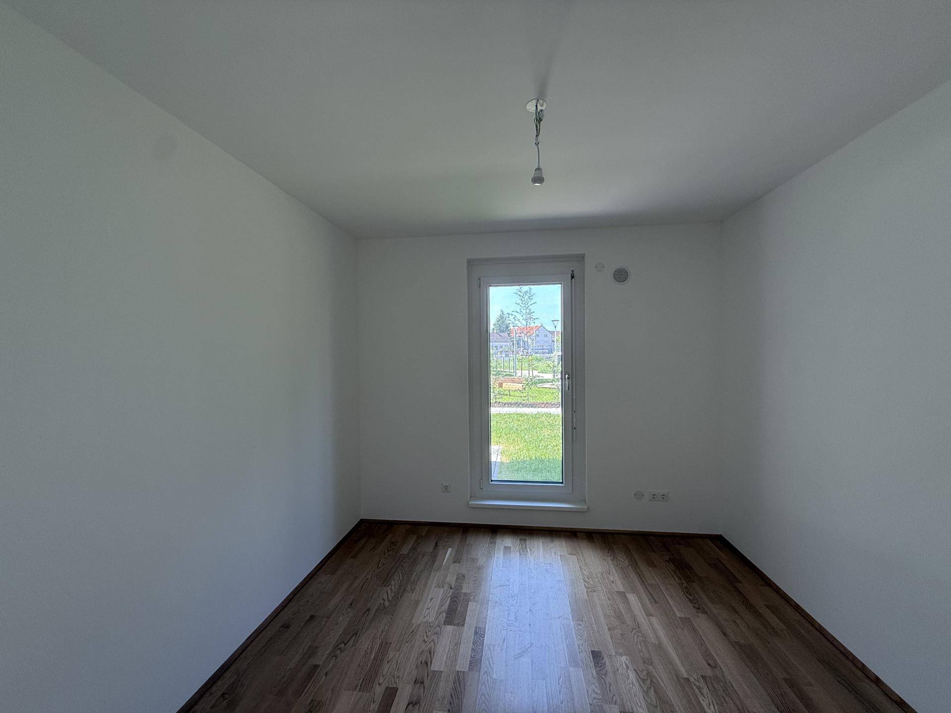 Helles, unmöbliertes Zimmer mit Holzboden und Fenster zum Außenbereich.