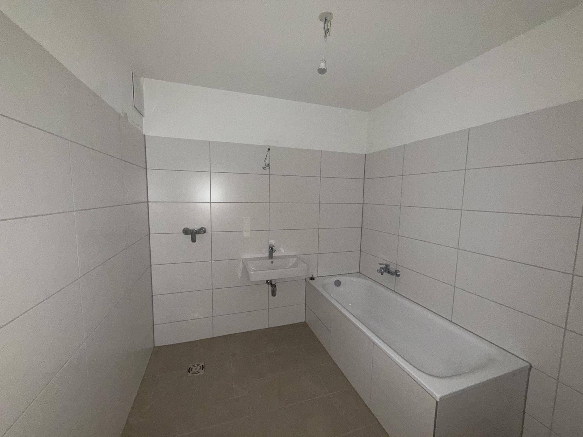 Unmöbliertes Badezimmer mit weißen Fliesen, Badewanne und Waschbecken.