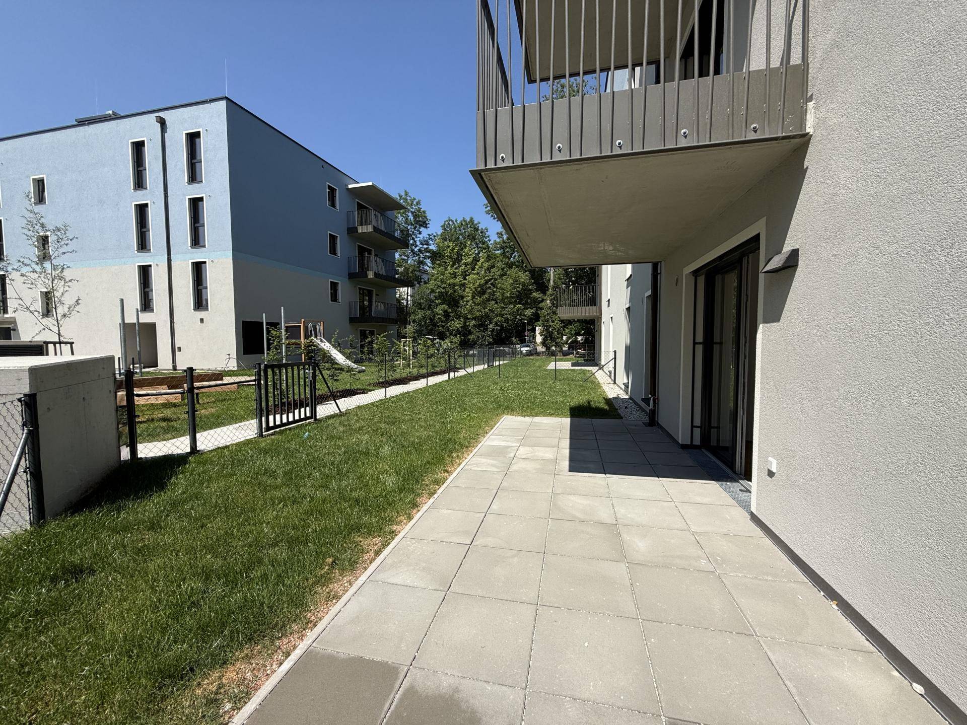 Geräumige Terrasse mit angrenzender Rasenfläche und Blick auf moderne Wohngebäude.