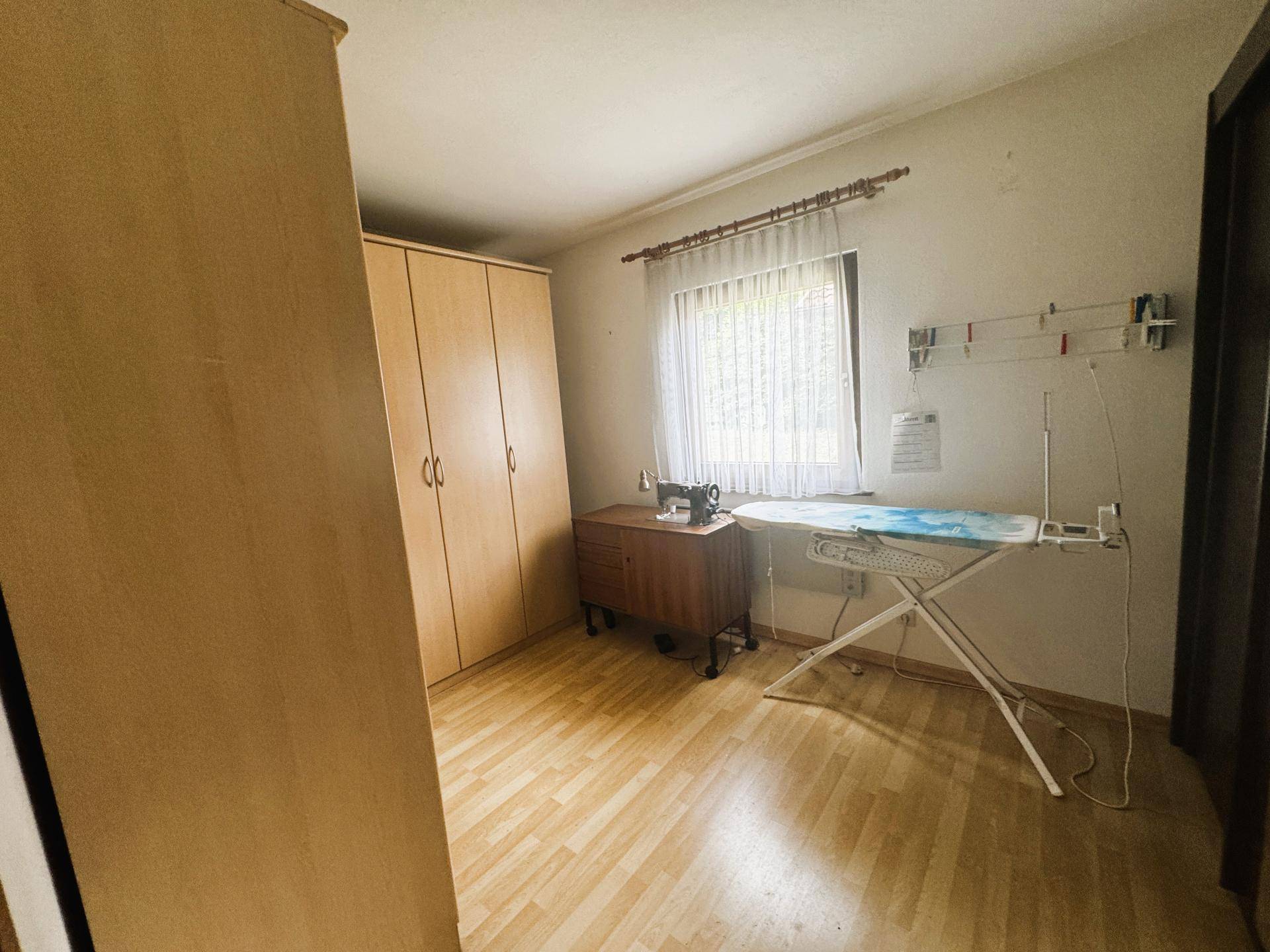 Helles Zimmer mit Schrank, Bügelbrett und Nähmaschine, vielseitig nutzbar als Hobbyraum.