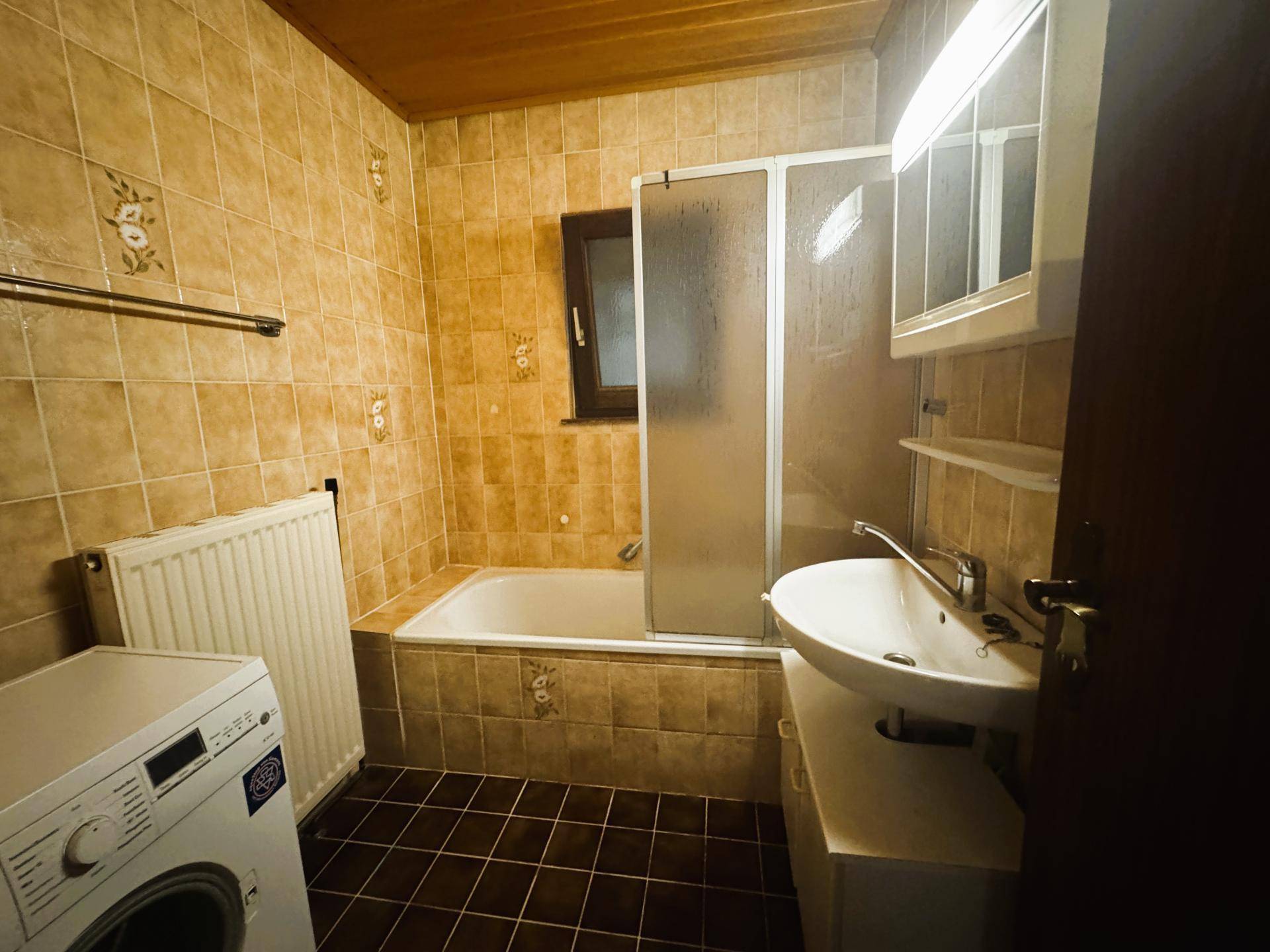 Gefliestes Badezimmer mit Badewanne, Duschabtrennung, Waschbecken und Fenster.