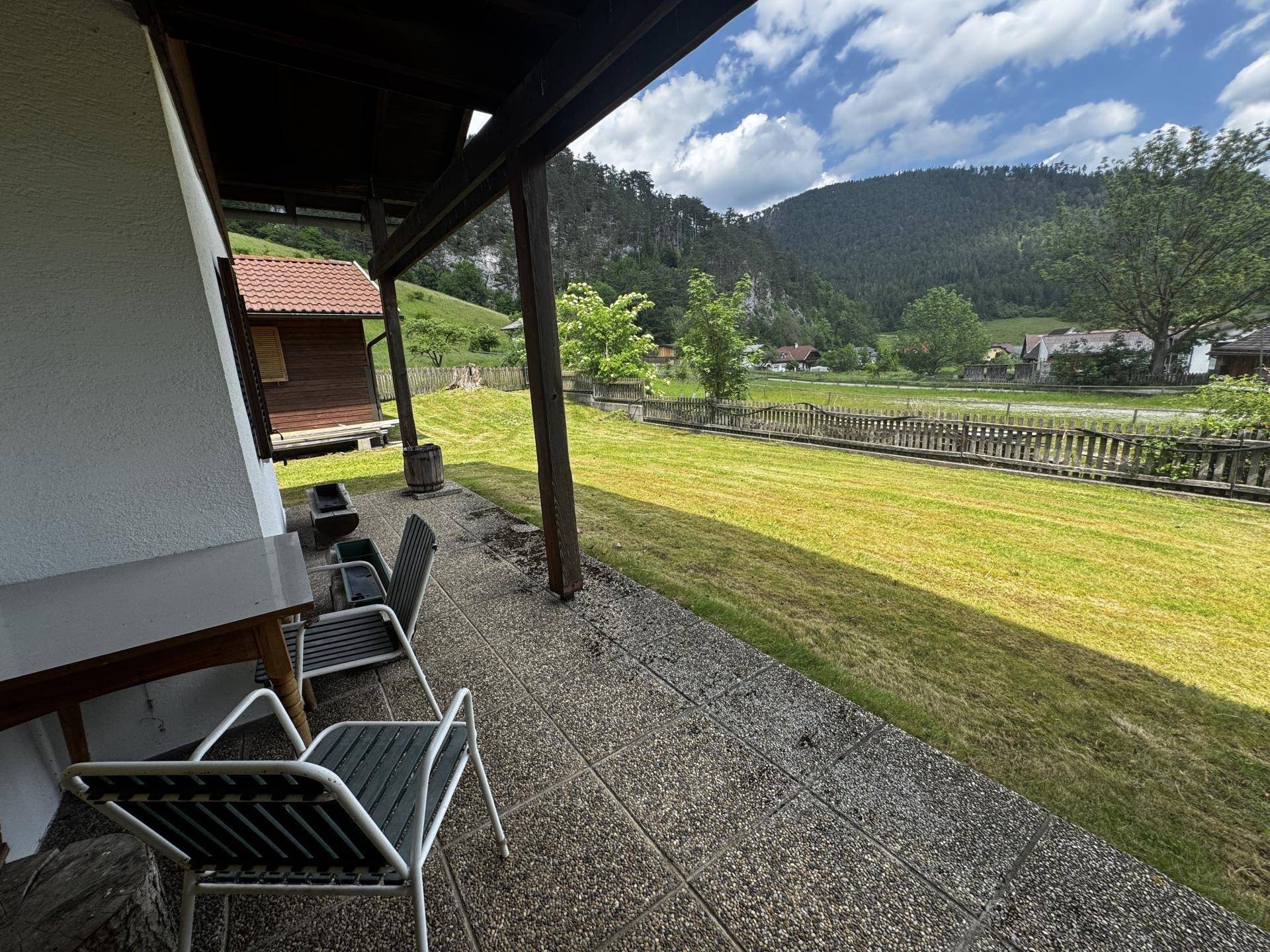 Überdachte Terrasse mit Sitzgelegenheiten und Blick auf die grüne Landschaft und Berge.