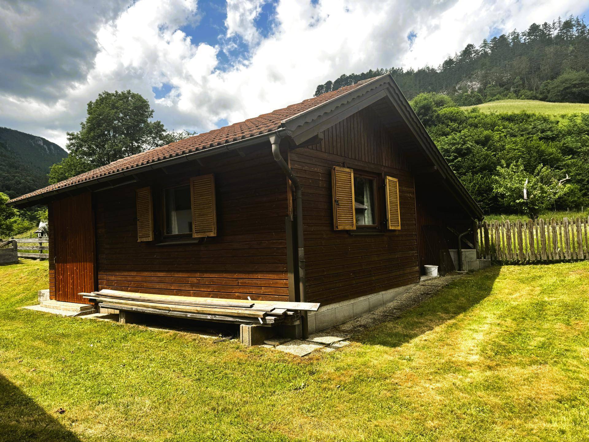 Kleine Holzhütte mit Satteldach im grünen Garten, umgeben von Natur.