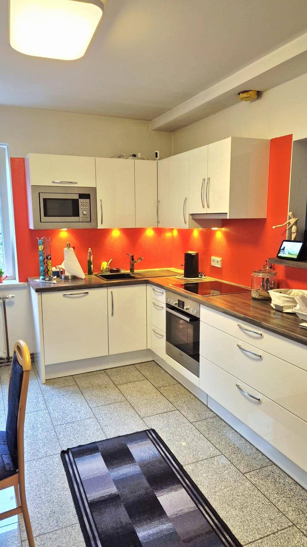 Helle Küche mit weißen Schränken, orangefarbener Rückwand und modernen Geräten.