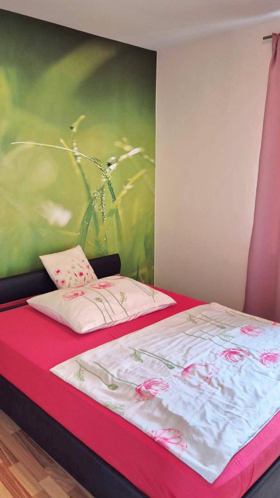 Schlafzimmer mit Bett und einer auffälligen grünen Tapete mit Naturmotiv.