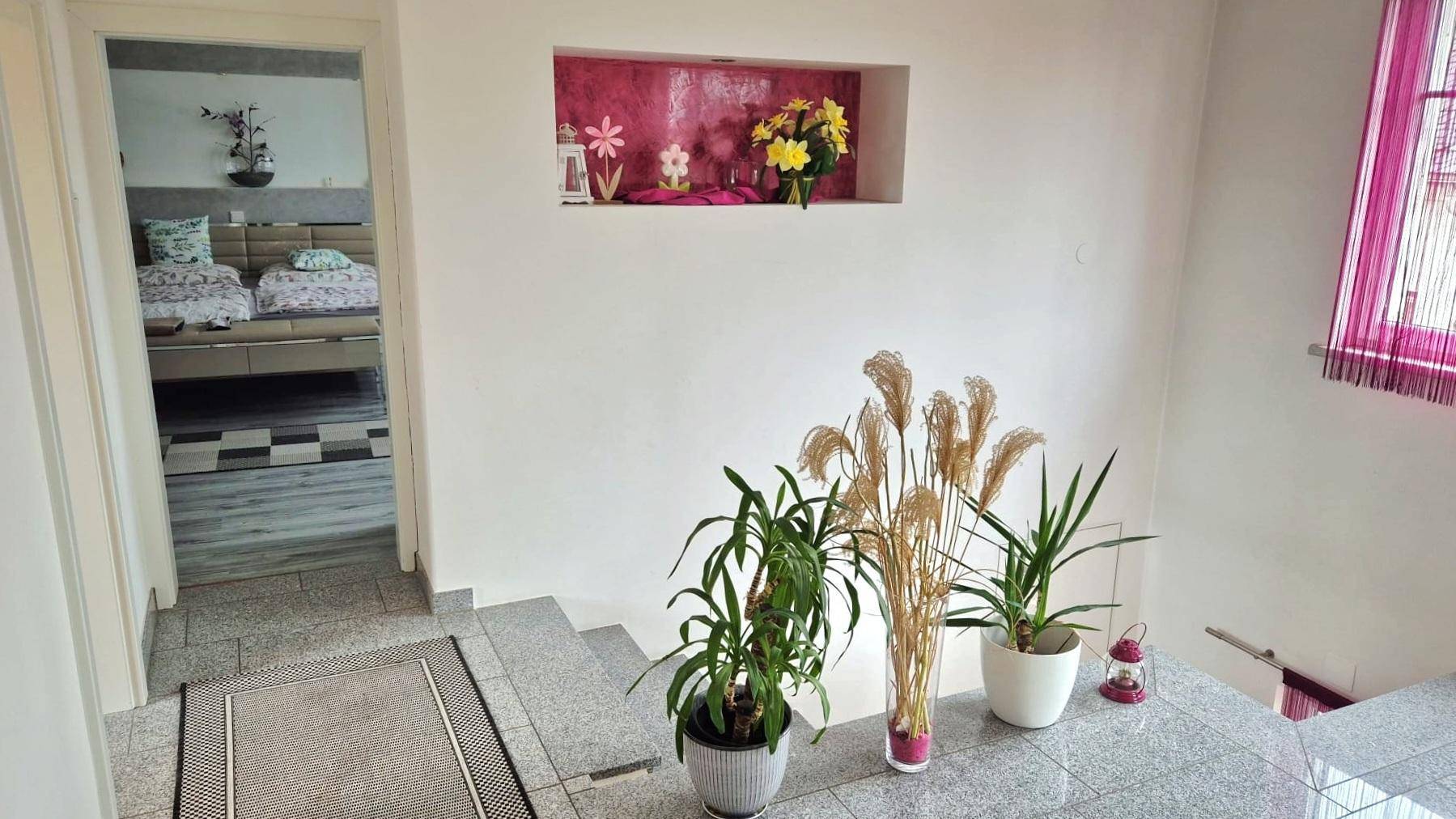 Heller Treppenabsatz mit Pflanzen und Blick in ein angrenzendes Schlafzimmer.