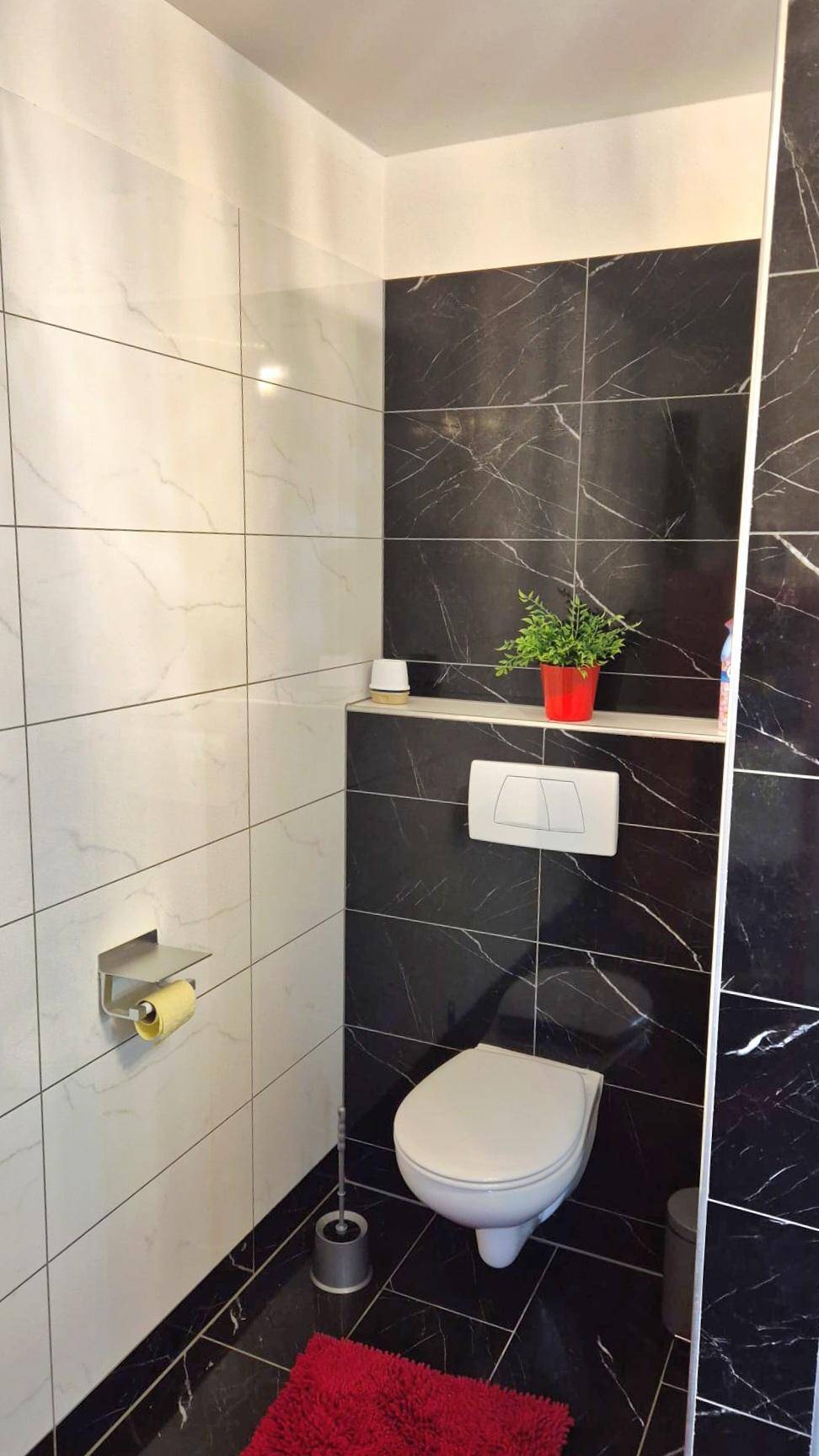 Separates WC mit wandhängender Toilette und stilvollen schwarz-weißen Fliesen.