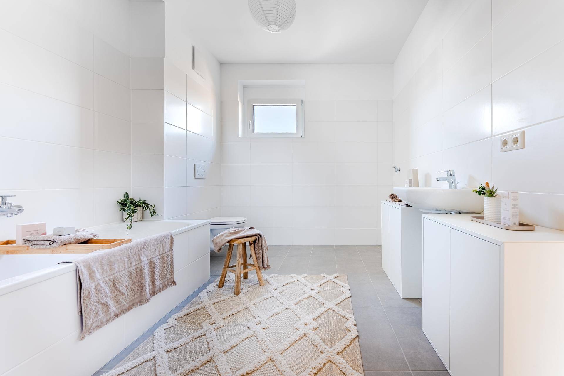 Helles Badezimmer mit Badewanne, WC, modernem Waschbecken und weißen Fliesen.