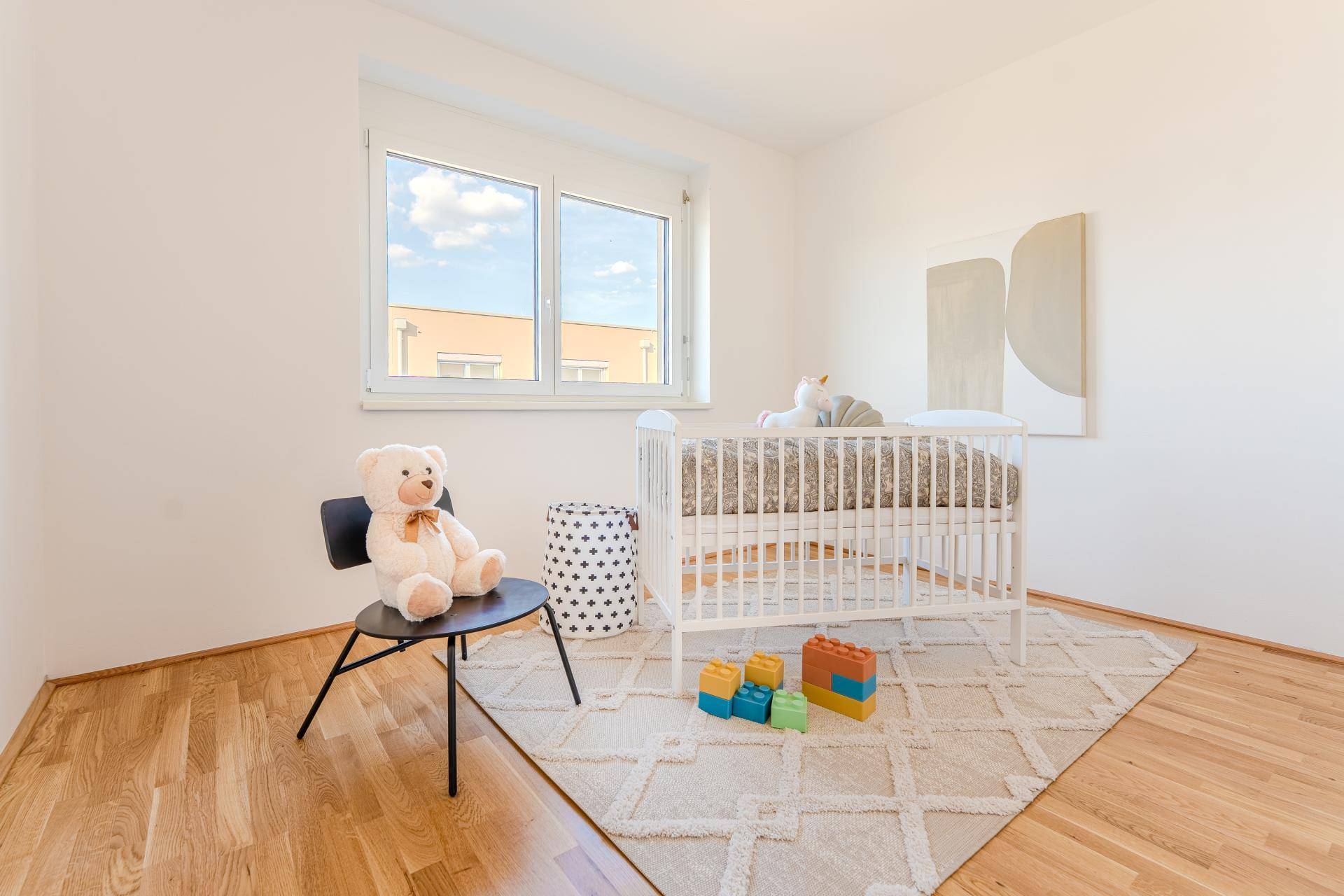 Helles Kinderzimmer mit Holzboden, Fenster und einem Babybett.