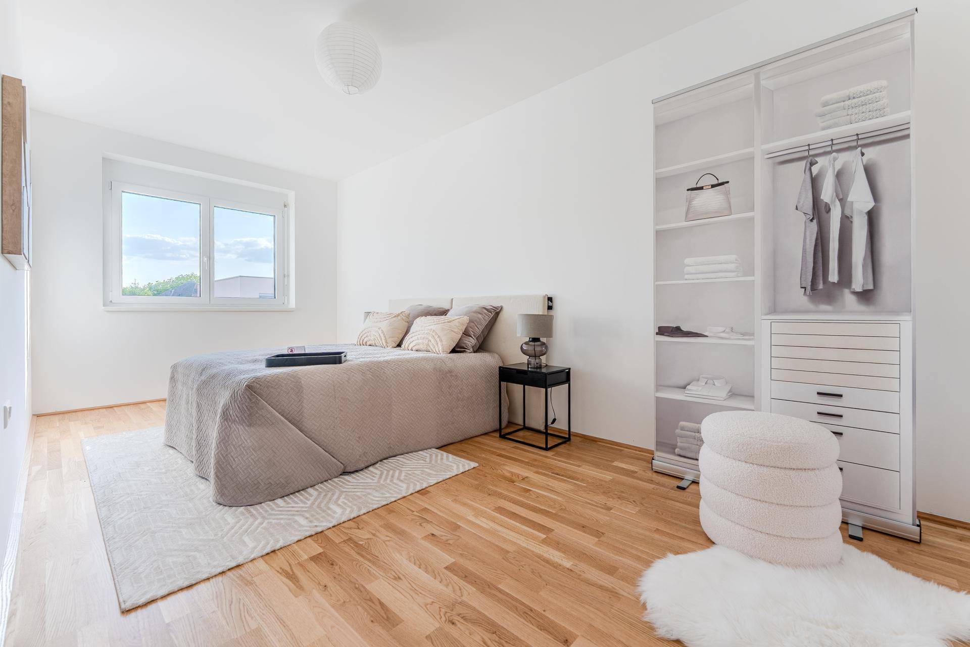 Helles Schlafzimmer mit Holzboden, großem Fenster und offenem Kleiderschrank.