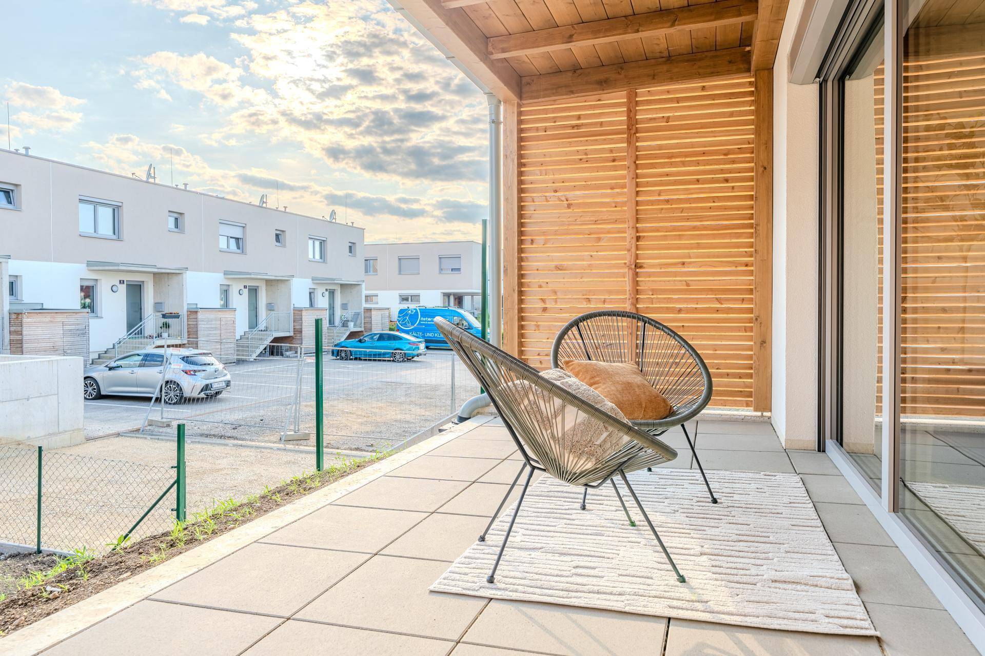 Geräumige Terrasse mit Fliesenboden und Sitzgelegenheiten, umgeben von Neubauten.
