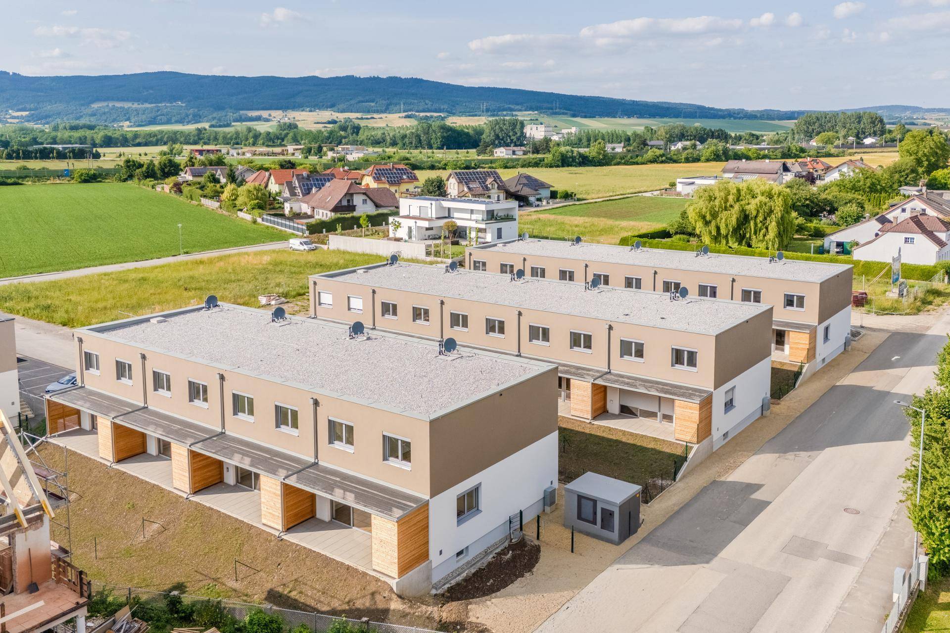Luftaufnahme einer modernen Reihenhaussiedlung in ländlicher Umgebung mit viel Grün.