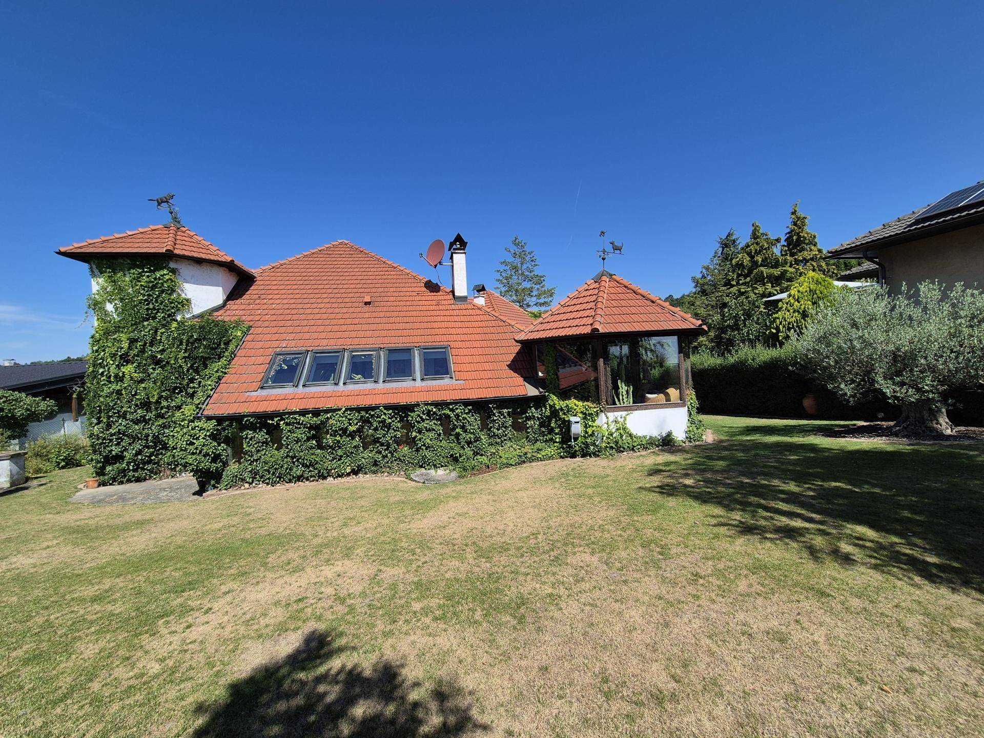Weitläufiger Garten mit Rasenfläche und einem charmanten Haus mit Ziegeldach und Wintergarten.