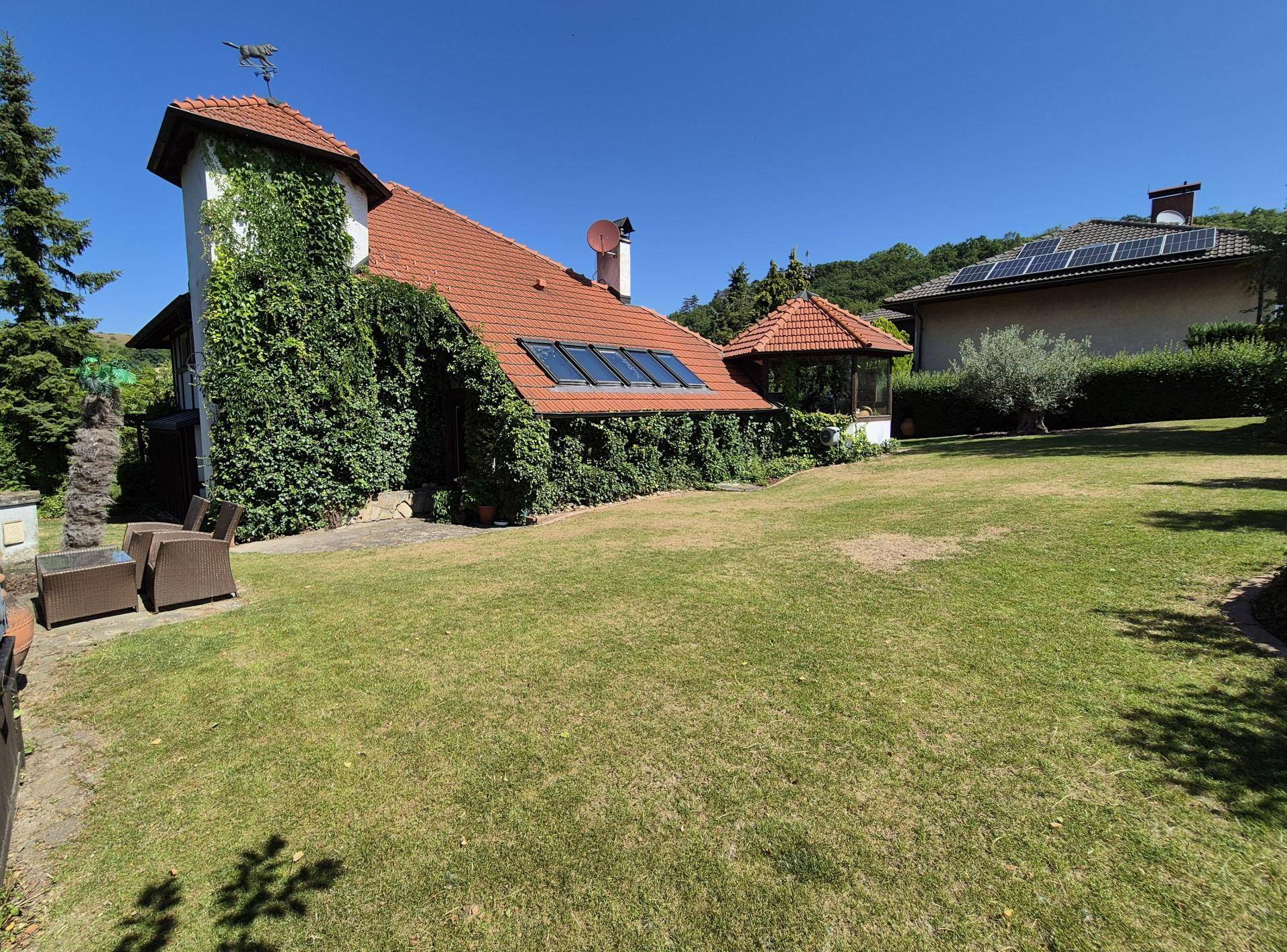 Charmantes Haus mit Efeubewuchs, Solaranlage auf dem Dach und großem Garten mit Sitzbereich.