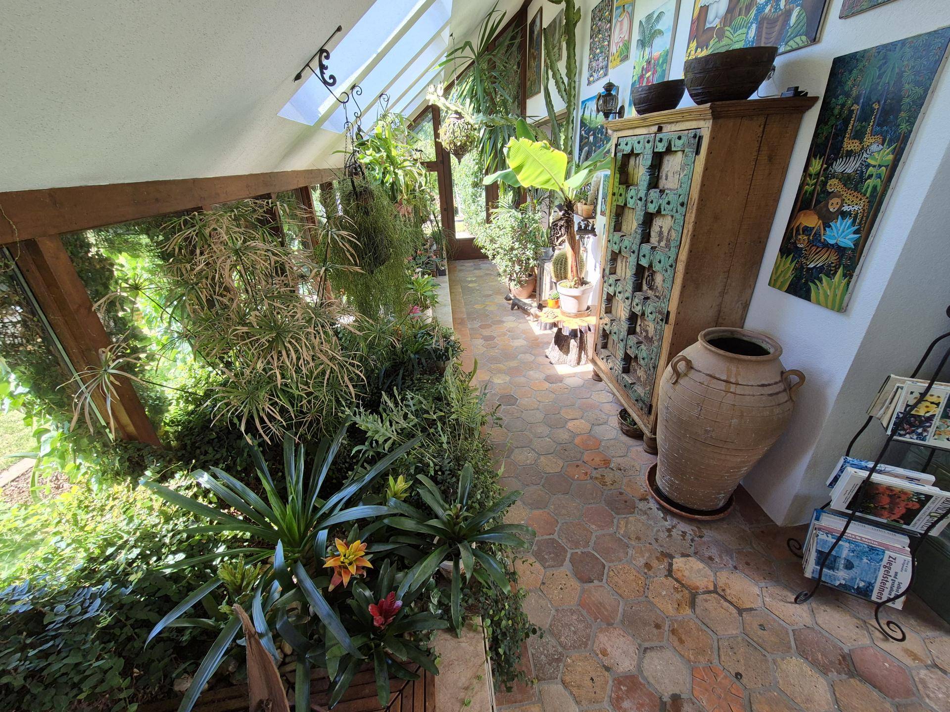 Heller Wintergarten mit üppigen Pflanzen, Terrakotta-Bodenfliesen und viel Tageslicht.