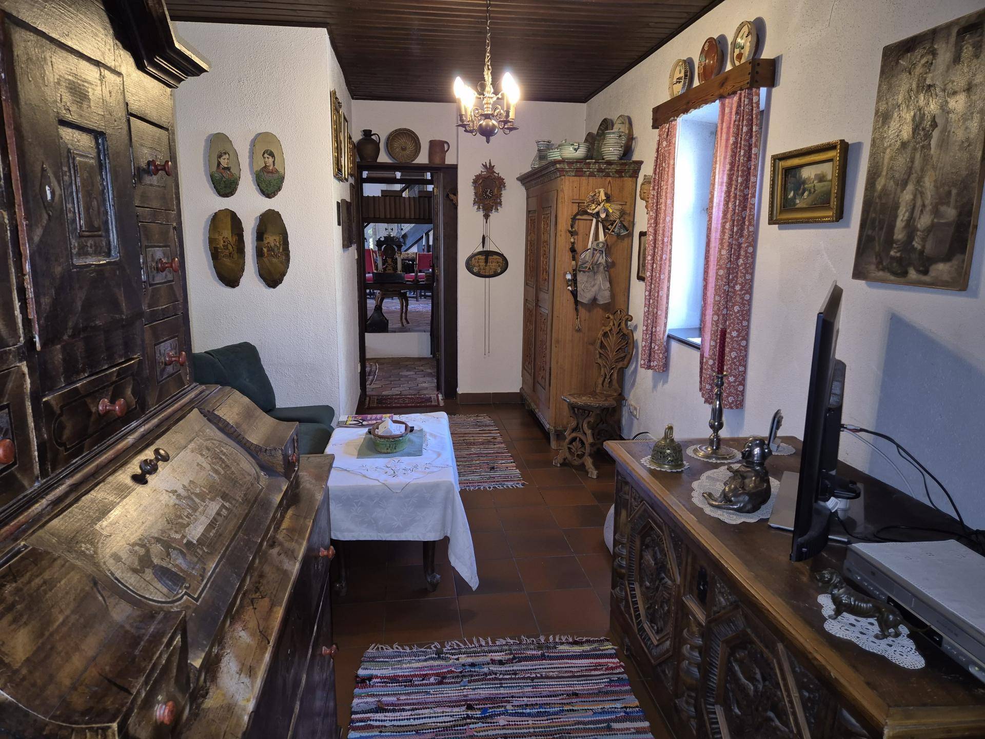 Gemütlicher Wohnraum mit traditionellen Holzmöbeln, Teppichen und einem kleinen Fenster.