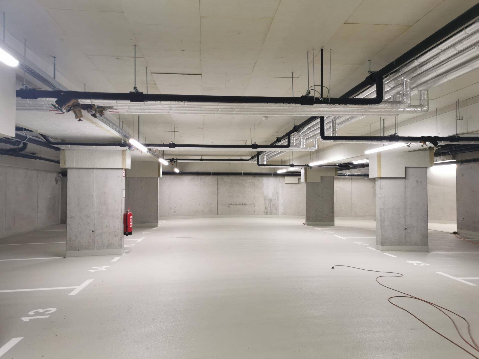 Geräumige Tiefgarage mit Betonboden und sichtbaren Installationen an der Decke.