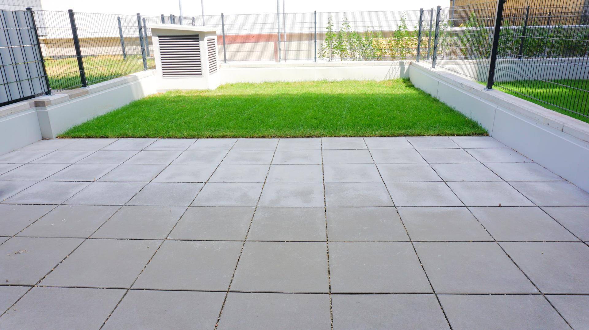 Gepflasterte Terrasse mit kleiner Rasenfläche und umzäuntem Bereich im Freien.