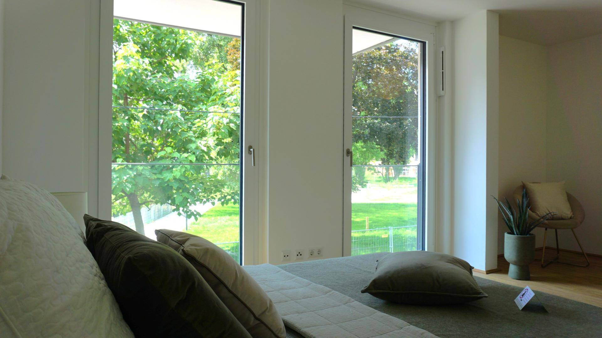 Schlafzimmer mit großen Fenstern und einem schönen grünen Ausblick auf Bäume und Wiese.