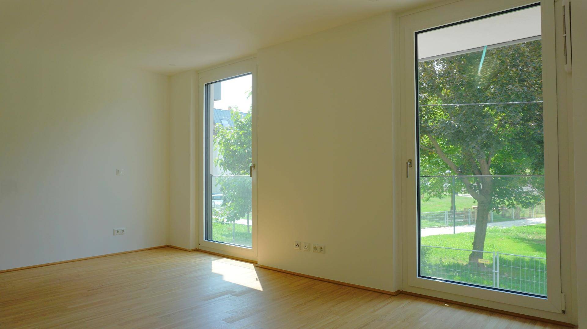 Heller, leerer Raum mit großen Fenstern und Blick ins Grüne, ideal als Schlaf- oder Arbeitszimmer.