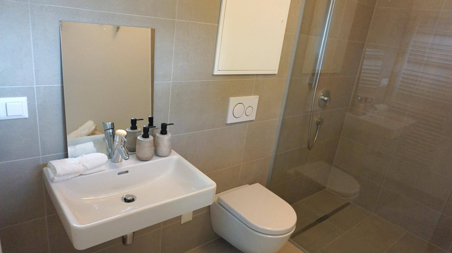 Modernes Badezimmer mit begehbarer Dusche, Wand-WC und hellen Fliesen.
