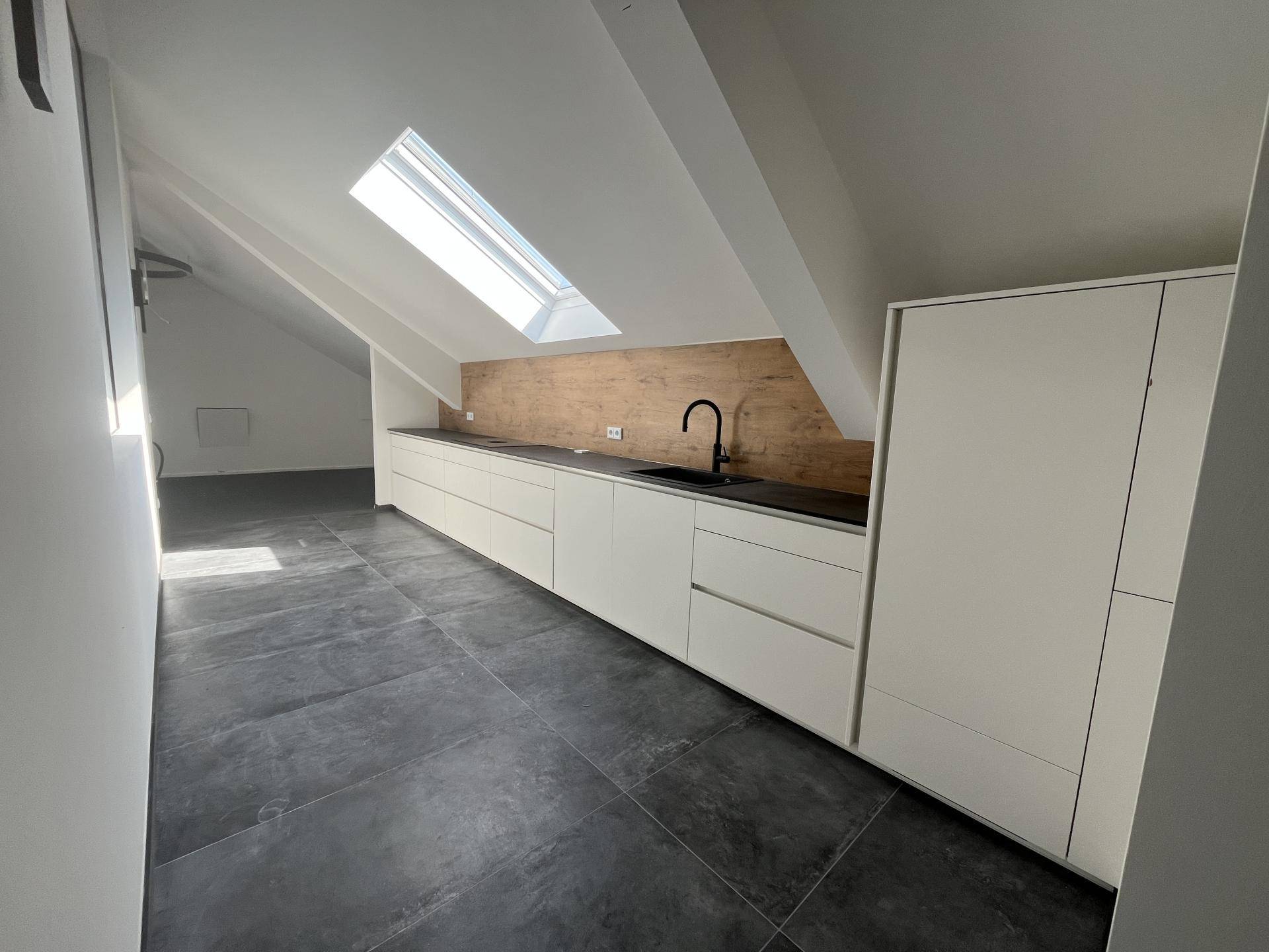 Helle Küchenzeile mit weißen Schränken, dunkler Arbeitsplatte und Dachfenster in modernem Raum.