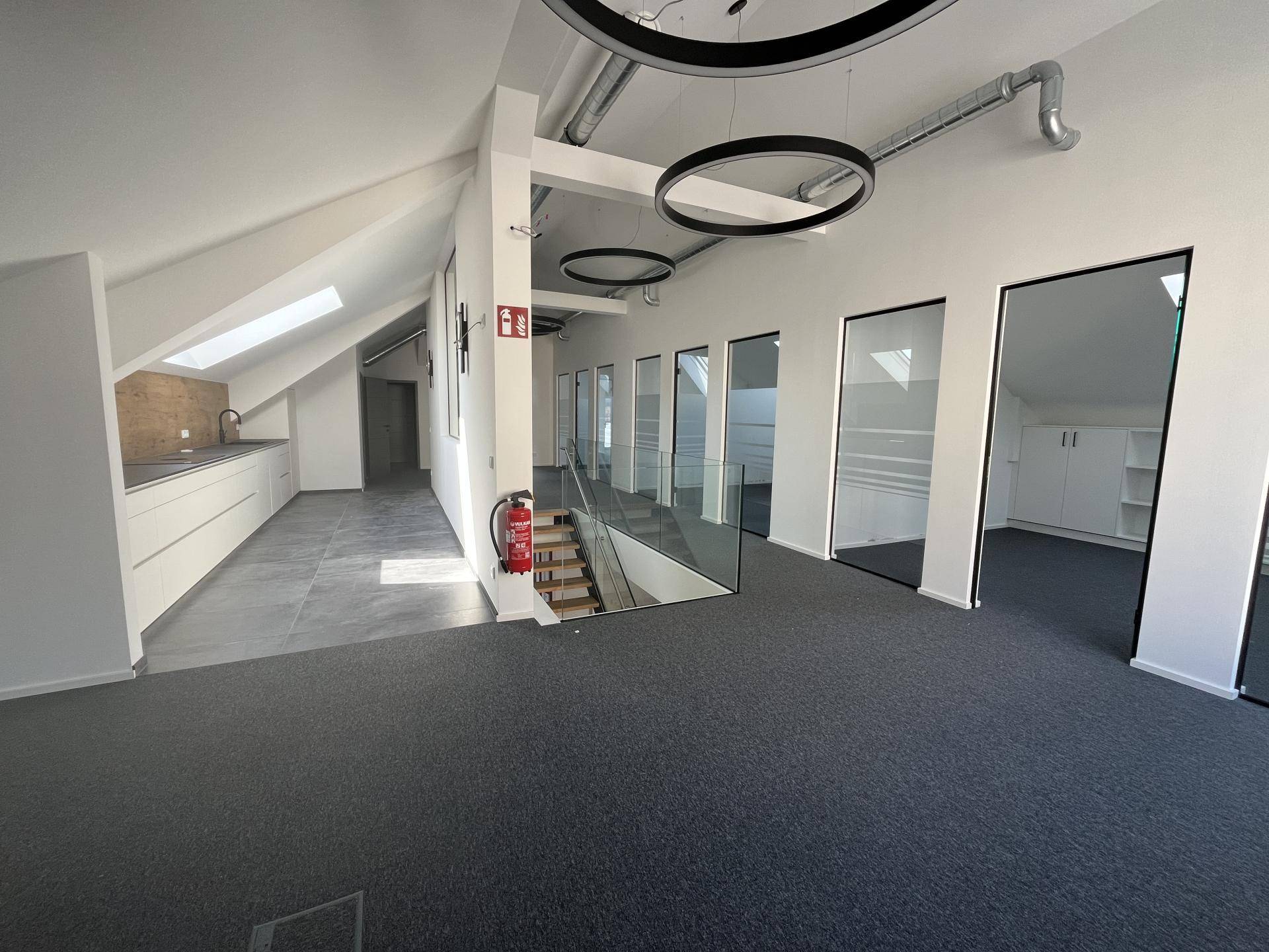 Heller Bürobereich im Obergeschoss mit Teppichboden, Glastüren und Blick zur Küchenzeile.
