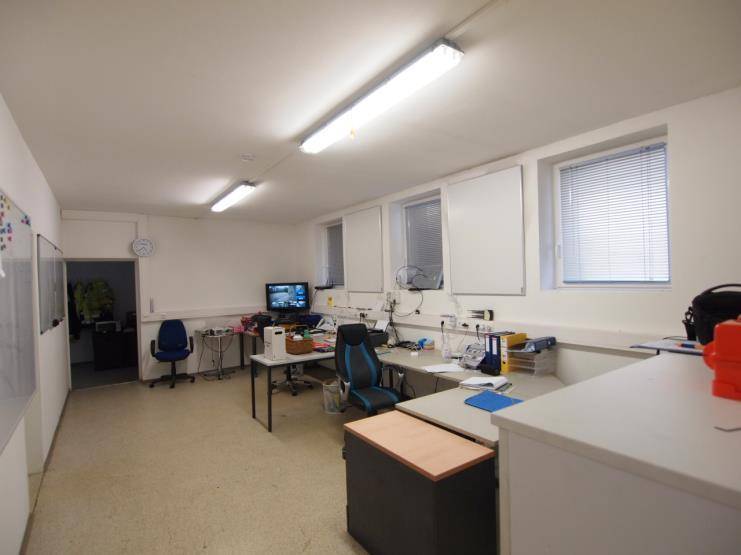 Ein funktionales Büro mit mehreren Schreibtischen, Computern und Fenstern mit Jalousien.