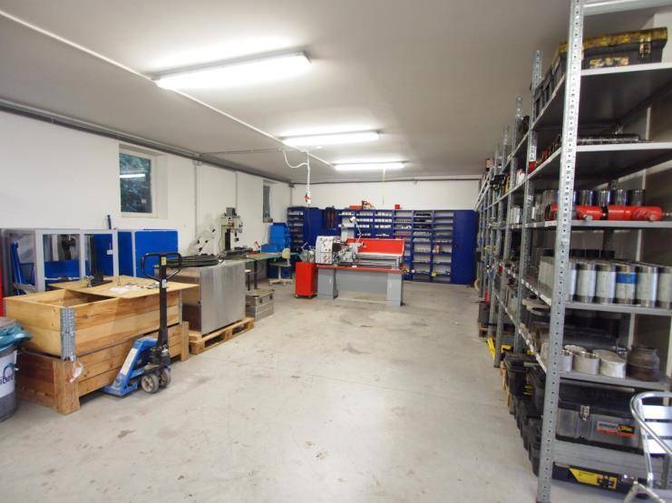 Geräumige Werkstatt mit Regalen voller Materialien, Werkbänken und industrieller Beleuchtung.