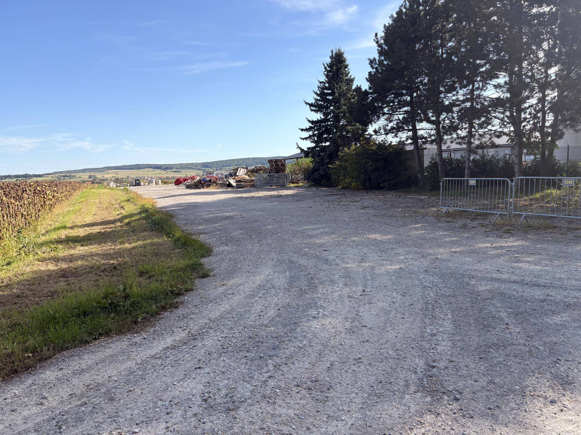 Kiesweg führt zu einem offenen Feld mit Blick auf die ländliche Umgebung und Bäume am Horizont.
