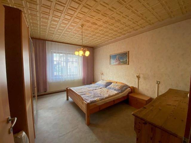 Schlafzimmer mit Doppelbett, Holzmöbeln und gemusterter Decke.