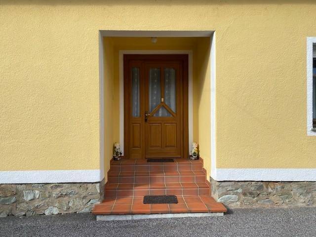 Eingangsbereich des Hauses mit Holztür, gefliesten Stufen und gelber Fassade.