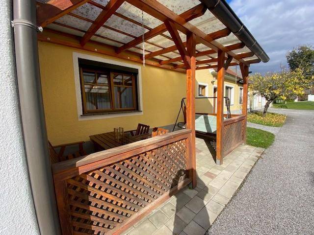 Überdachte Terrasse mit Holzpergola, Sitzgelegenheiten und Blick auf den Vorplatz.