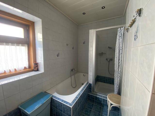 Badezimmer mit Badewanne, Dusche, Fenster und blauen Fliesen.