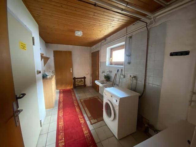 Hauswirtschaftsraum im Keller mit Waschmaschine, Waschbecken und Fliesenboden.
