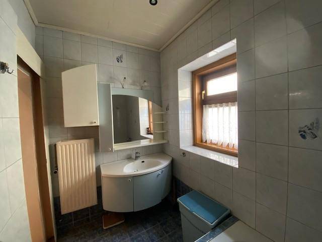 Badezimmer mit Waschbecken, Spiegelschrank, Heizkörper und Fenster.
