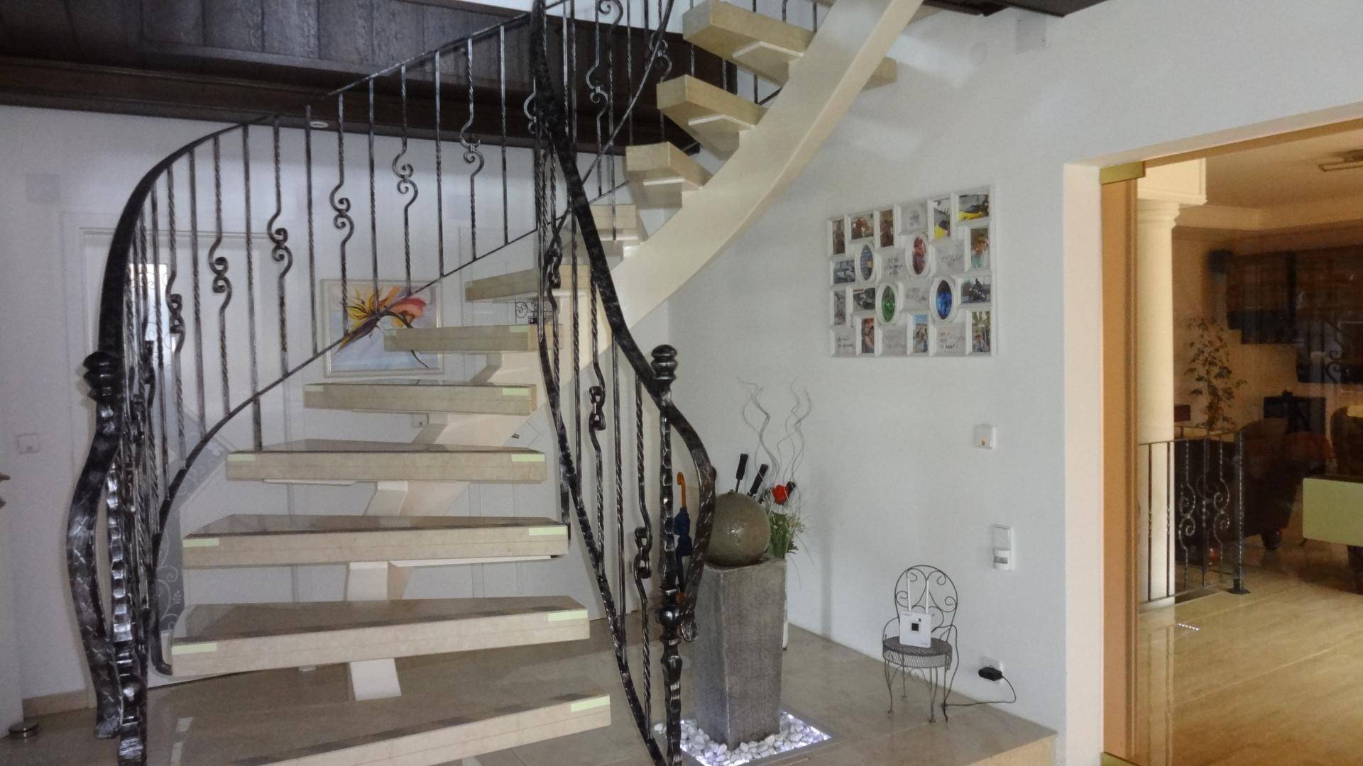 Elegante Wendeltreppe mit schmiedeeisernem Geländer in einem hellen Eingangsbereich.
