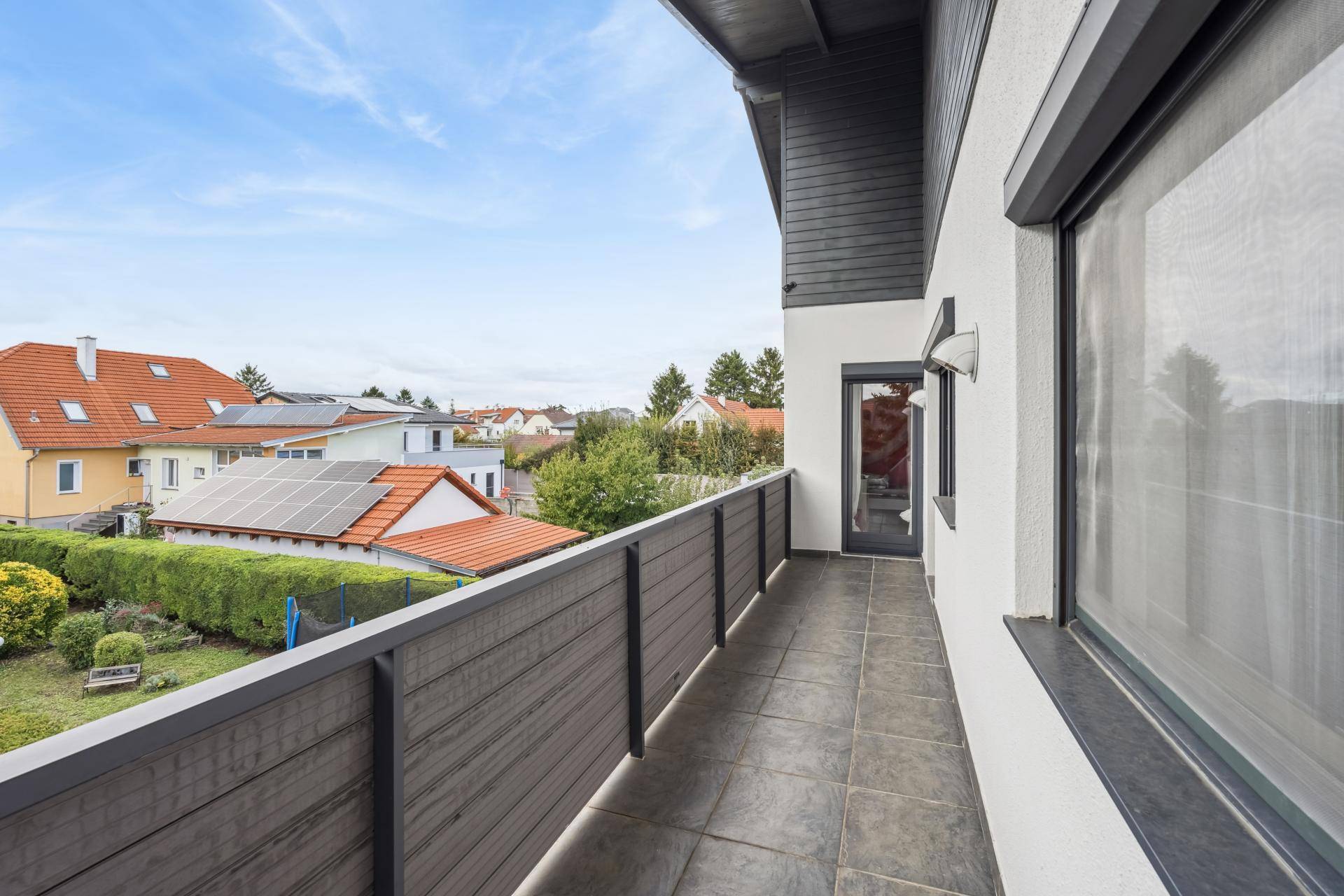Langer Balkon mit Fliesenboden und Blick auf die umliegenden Häuser und Gärten.