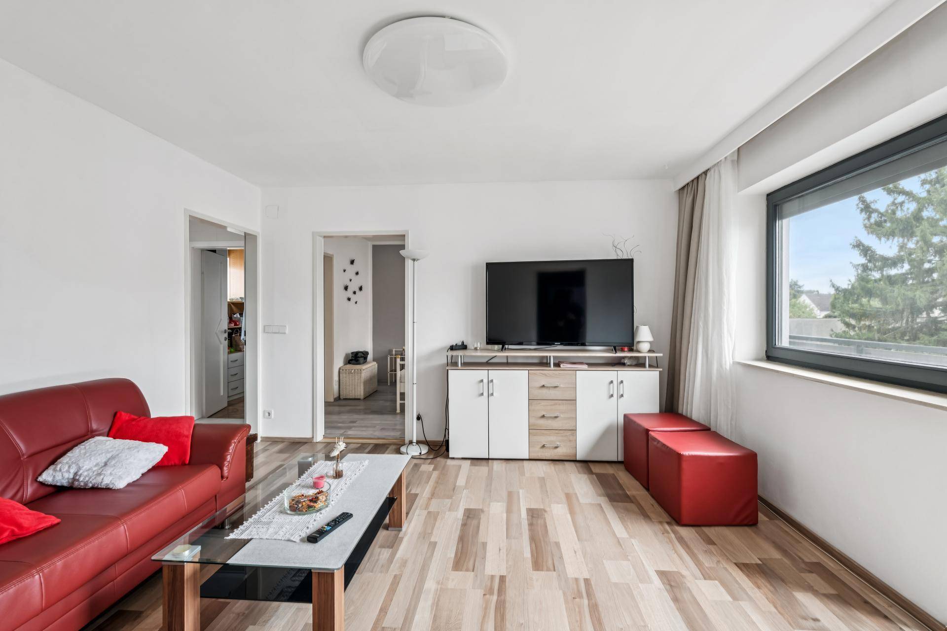 Gemütliches Wohnzimmer mit rotem Sofa, Holzboden und großem Fenster.
