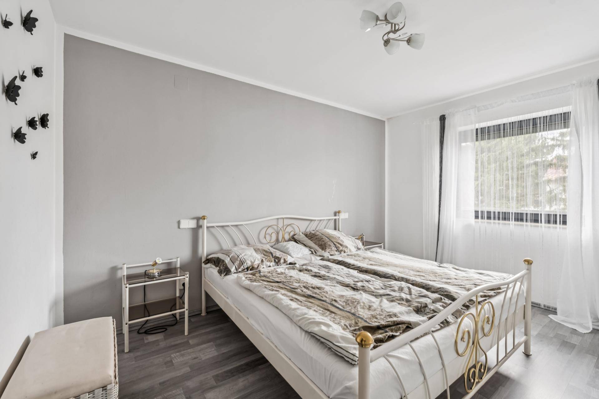 Helles Schlafzimmer mit grau gestrichener Wand, Doppelbett und Laminatboden.