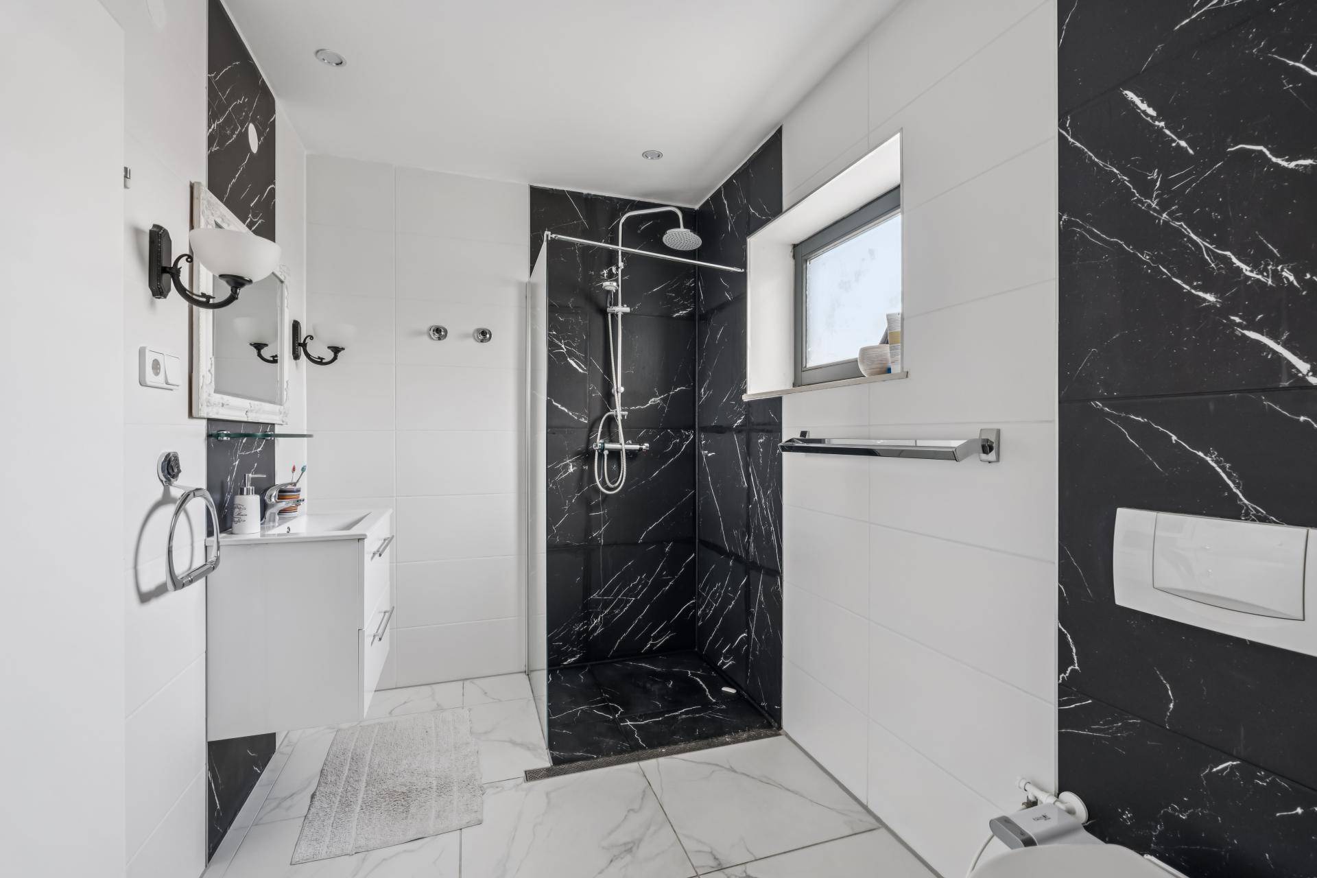 Modernes Badezimmer mit schwarz-weißen Marmorfliesen, Dusche und Fenster.