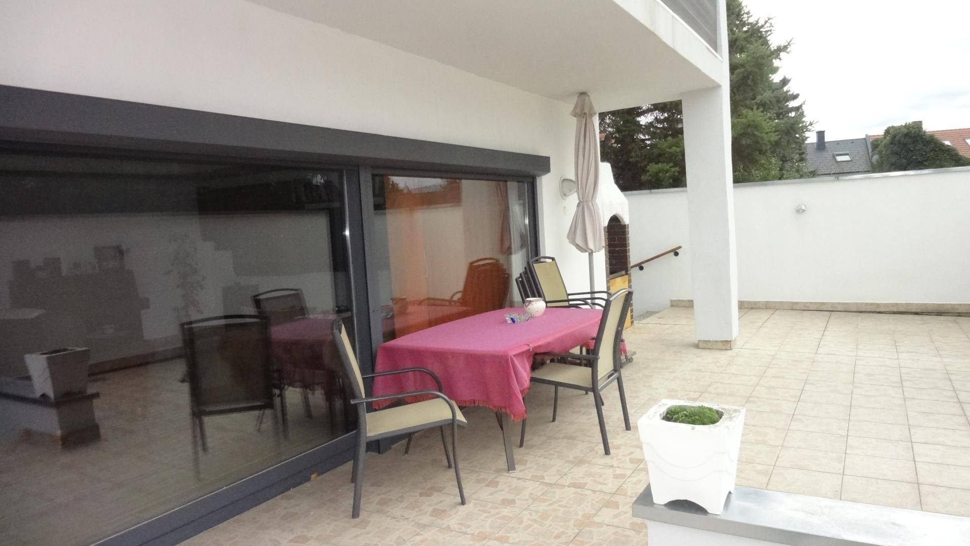Große geflieste Terrasse mit Esstisch, Stühlen und Grillbereich.