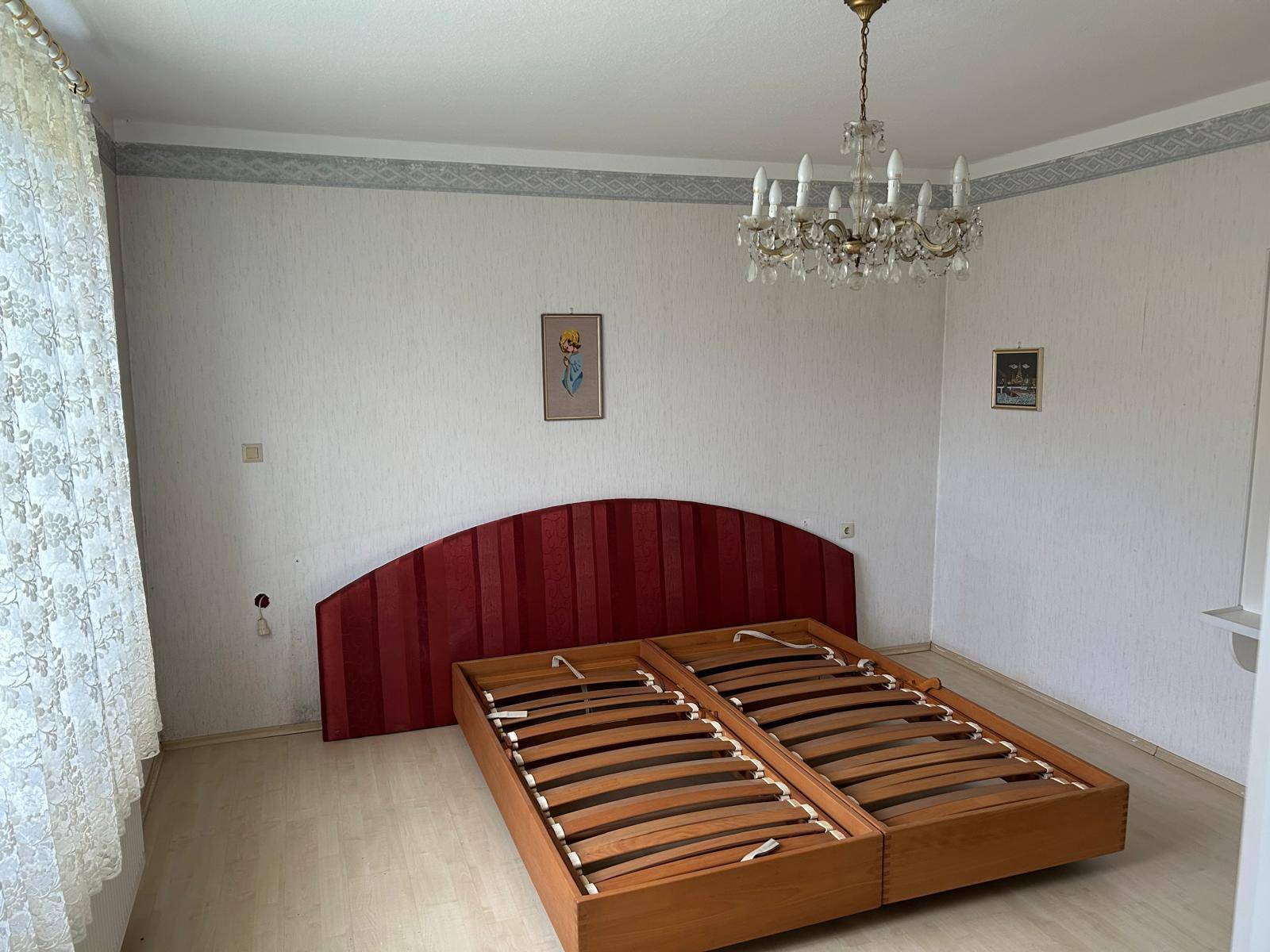 Schlafzimmer mit Holzbettrahmen, rotem Kopfteil und Kronleuchter an der Decke.