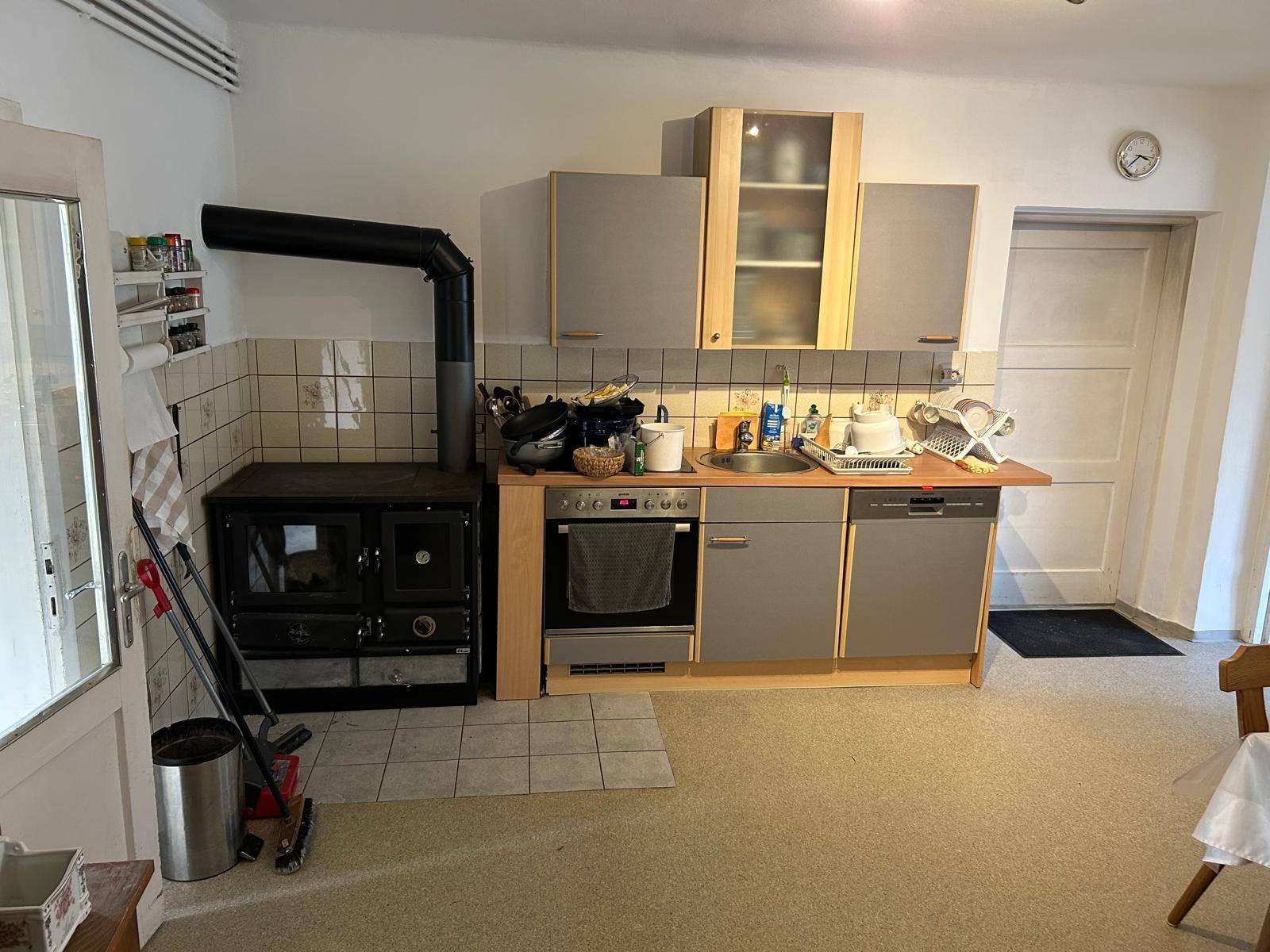 Rustikale Küche mit Holzofen, grauen Schränken und funktionaler Ausstattung.